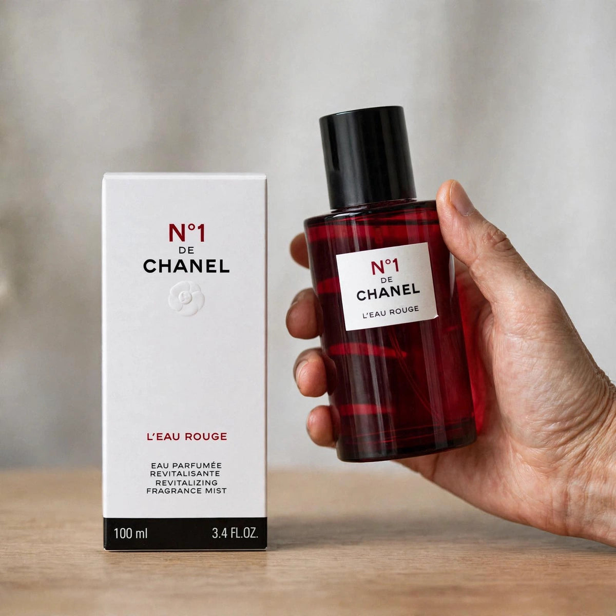 Hand holding Chanel No 1 L'Eau Rouge fragrance mist bottle